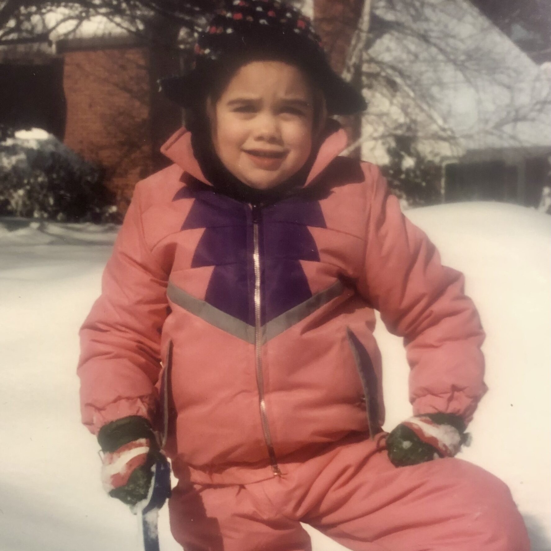 A young girl in pink snow suit holding ski poles.