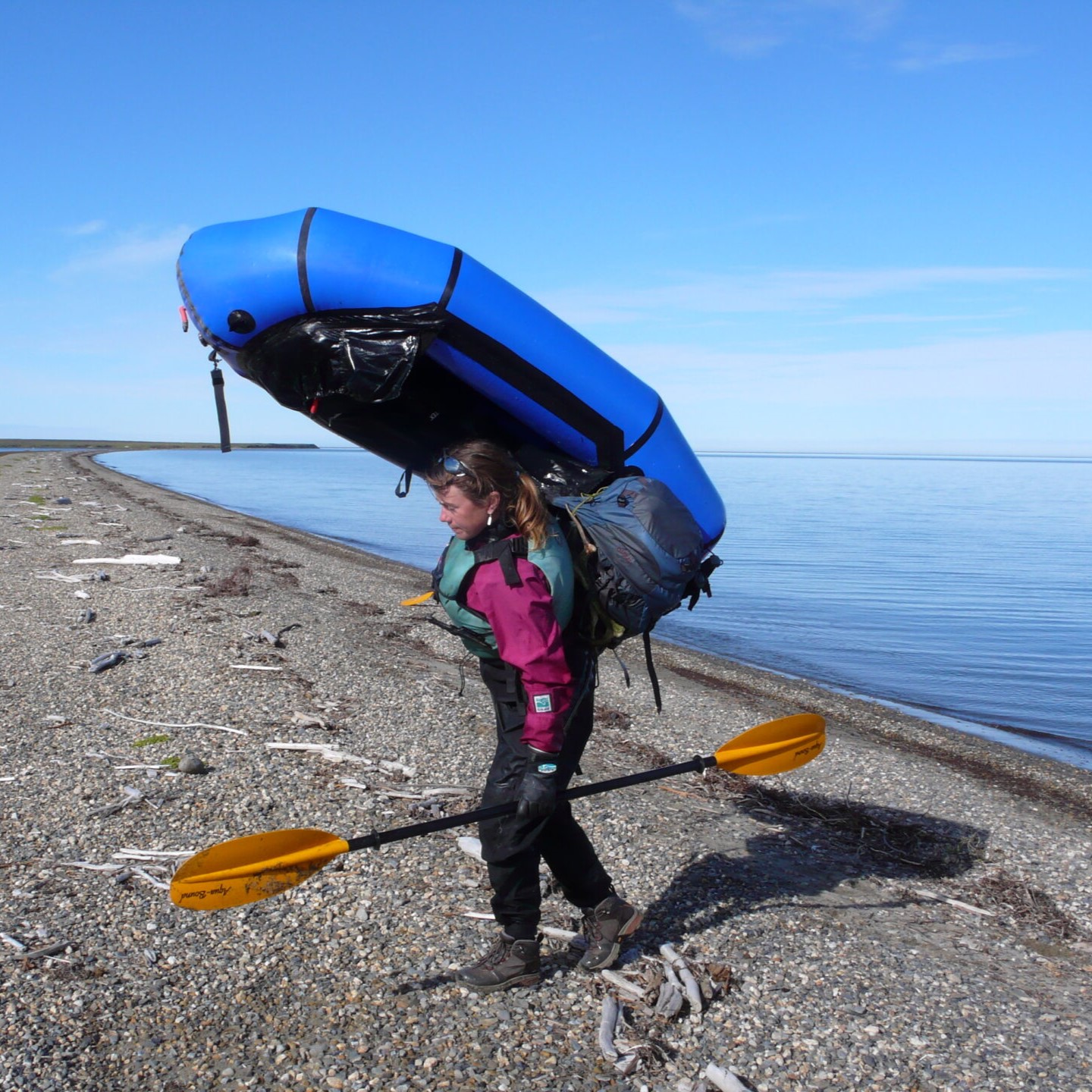 A woman carrying two oars and a boat on the beach.